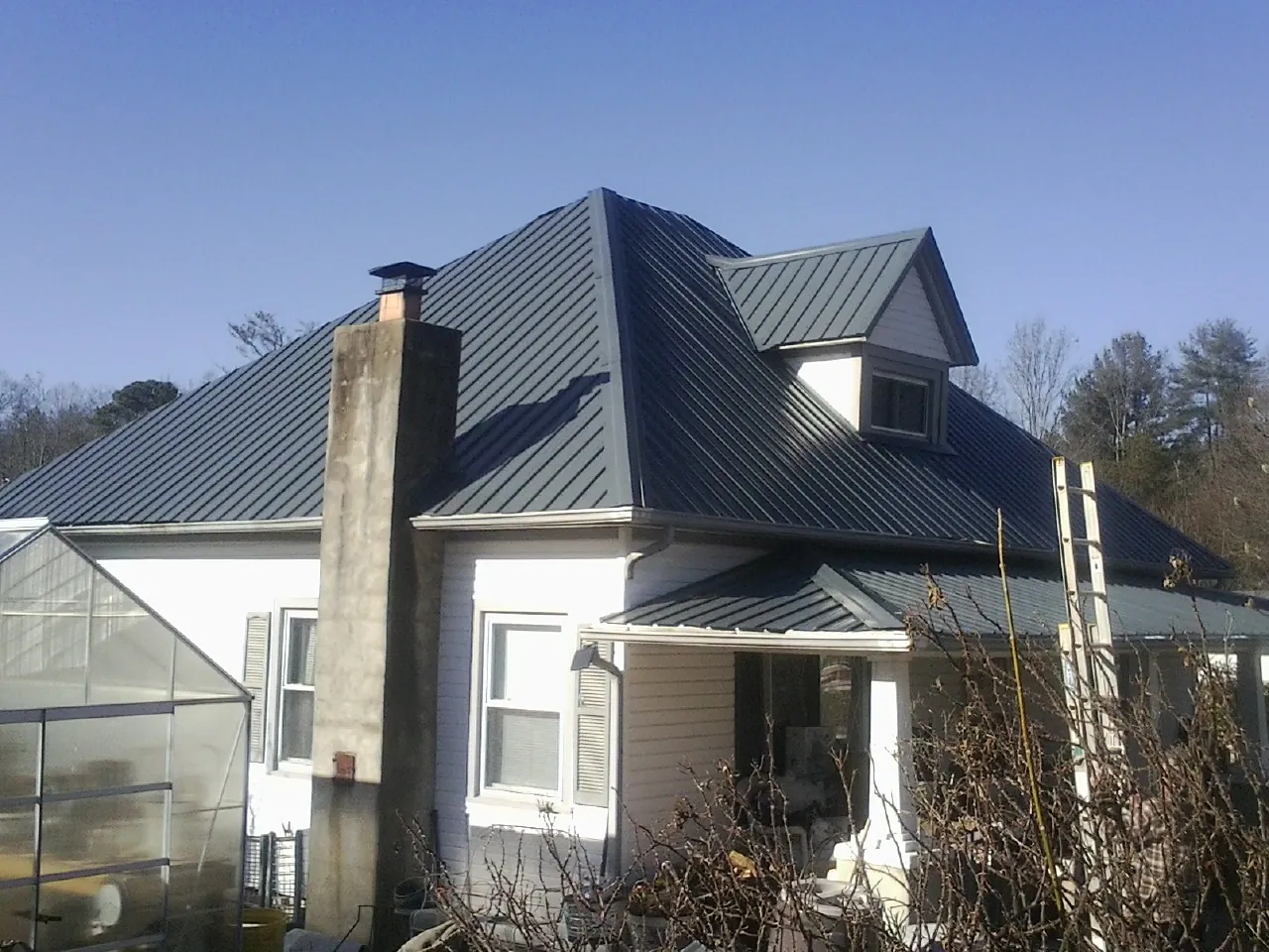 Dark blue standing seam metal roof on a white farmhouse with dormer — Slate & Tile Roof Repair by Roofing Brothers in Woodsville