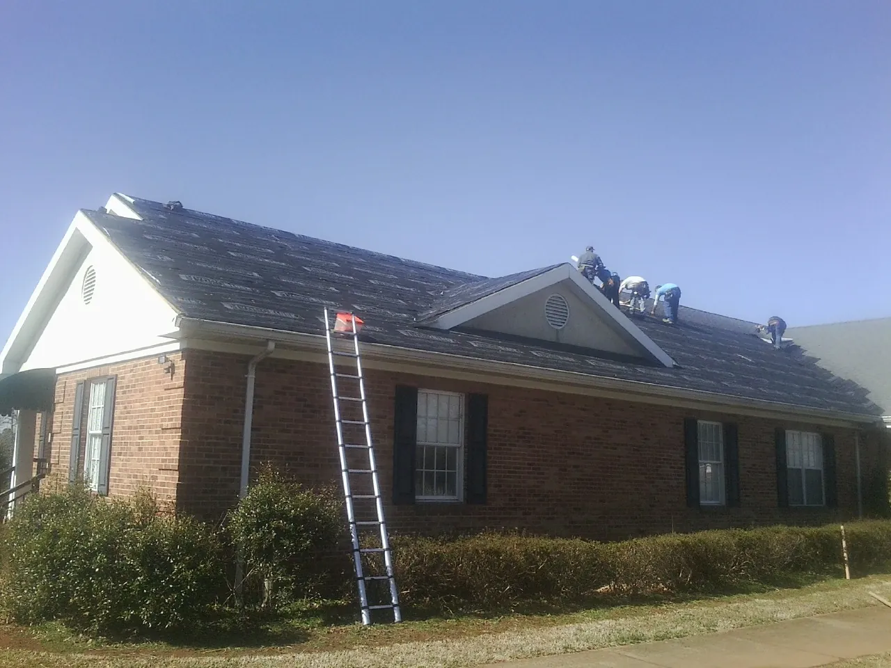 Crew tearing shingles off a brick ranch roof with a ladder set — Emergency Roof Repair work by our crew in Woodsville