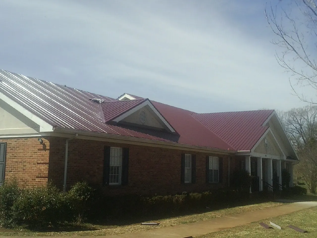 Red metal roof with gabled entries on a long brick building, from a Hail Damage Roof Repair job in Woodsville