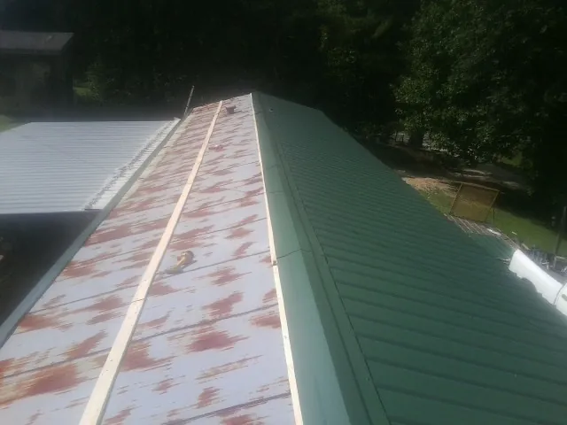 Old rusted panels beside newly installed green metal roofing — Wind Damage Roof Repair by Roofing Brothers in Woodsville