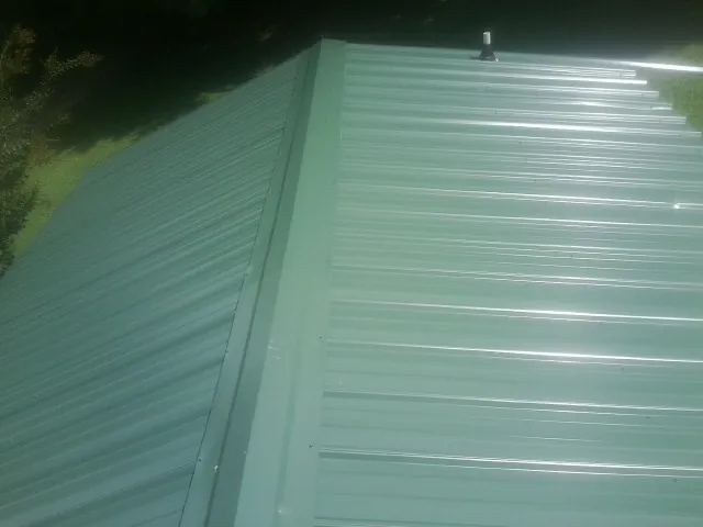 New green metal panels meeting at the ridge of a roof — Flat Roof Repair work by our crew in Woodsville