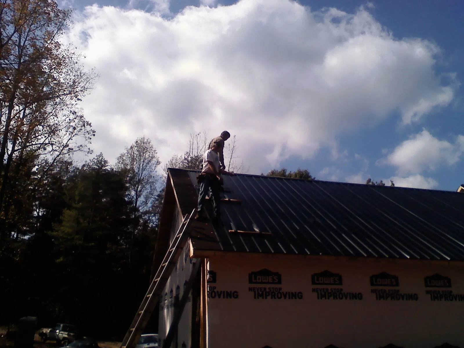 Roofer fastening dark metal panels high against a cloudy sky, from a Roof Inspection job in Woodsville