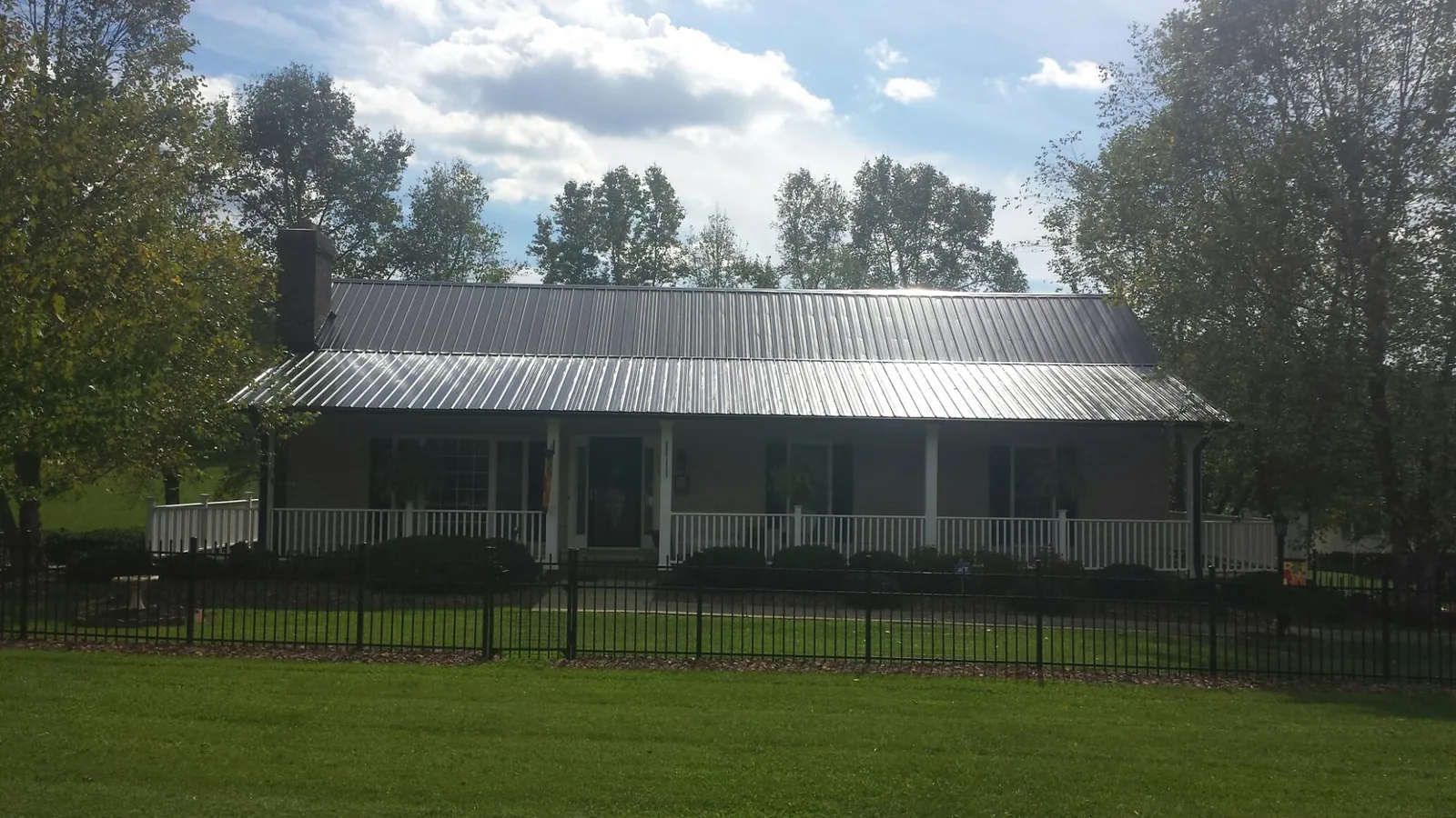 Gray metal roof on a brick ranch with a full width front porch — Gutter Guard Installation work by our crew in Woodsville