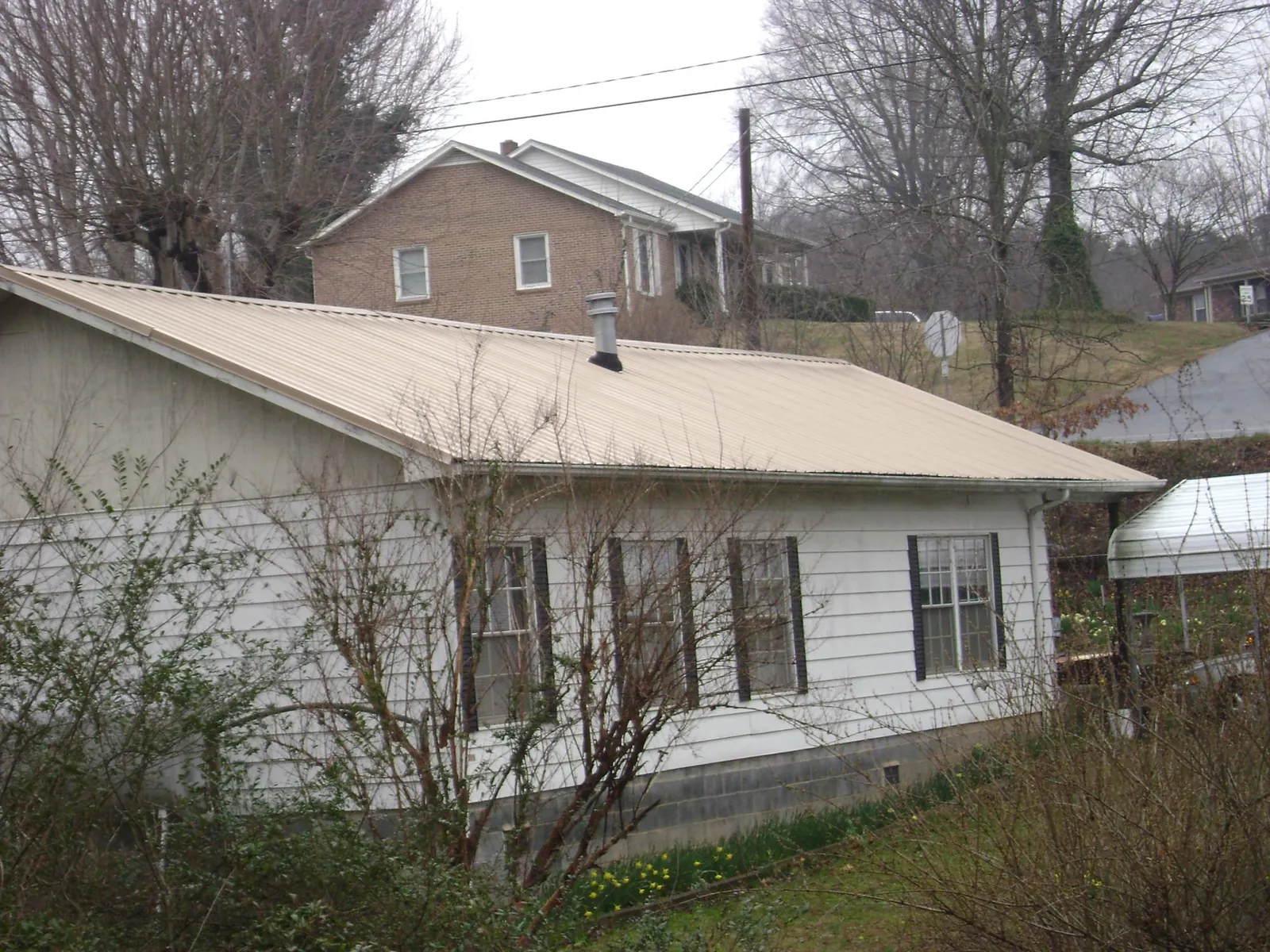 Tan metal roof on a white sided house set into a hillside — Commercial Roofing by Roofing Brothers in Woodsville