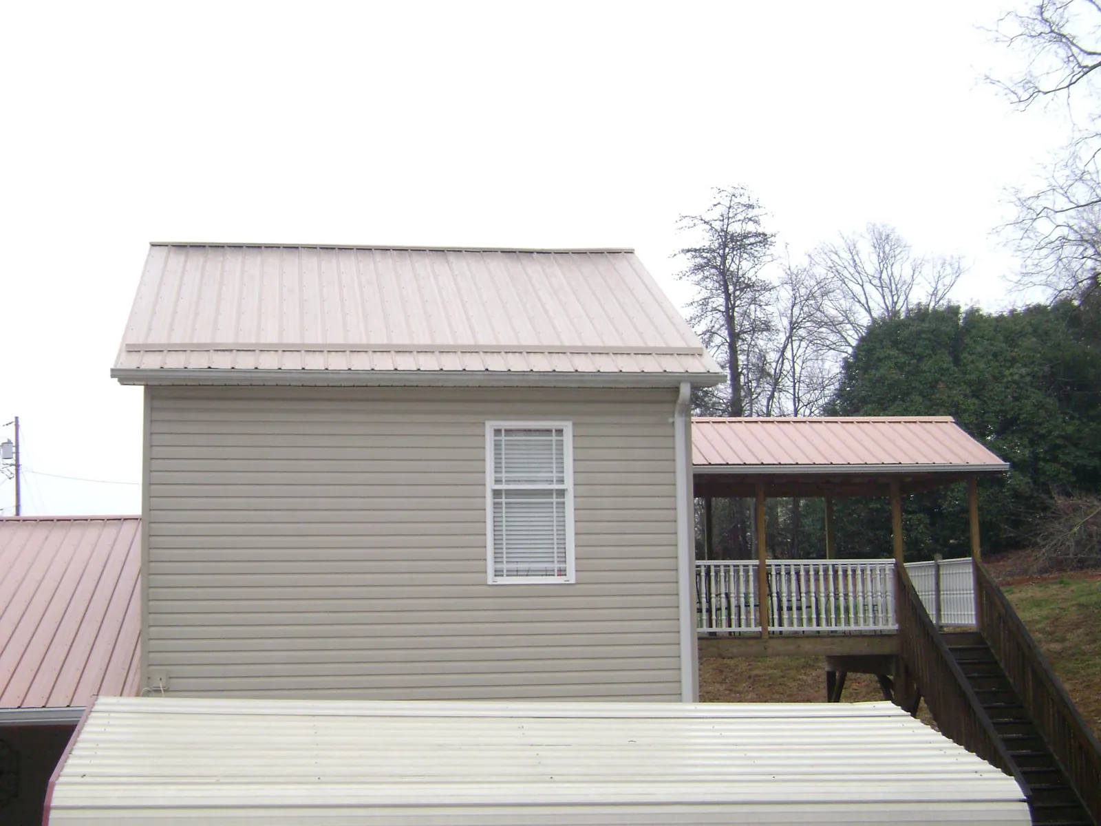 Tan metal roofs on a two story addition and attached porch, from a Roof Replacement job in Woodsville